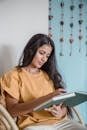 Woman sitting in a chair, reading a book indoors, creating a calm and relaxed atmosphere.
